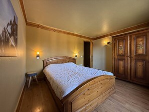 Ein Schlafzimmer mit einem hölzernen Bett, zwei Wandleuchten, einer Tür mit floralem Dekor und einem kleinen Hocker.