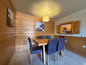 A dining area with a wooden table and chairs, a hanging light fixture, and a kitchen area with wooden cabinets. - Ski-in/ski-out apartment - 6 guests (Belle Plagne)