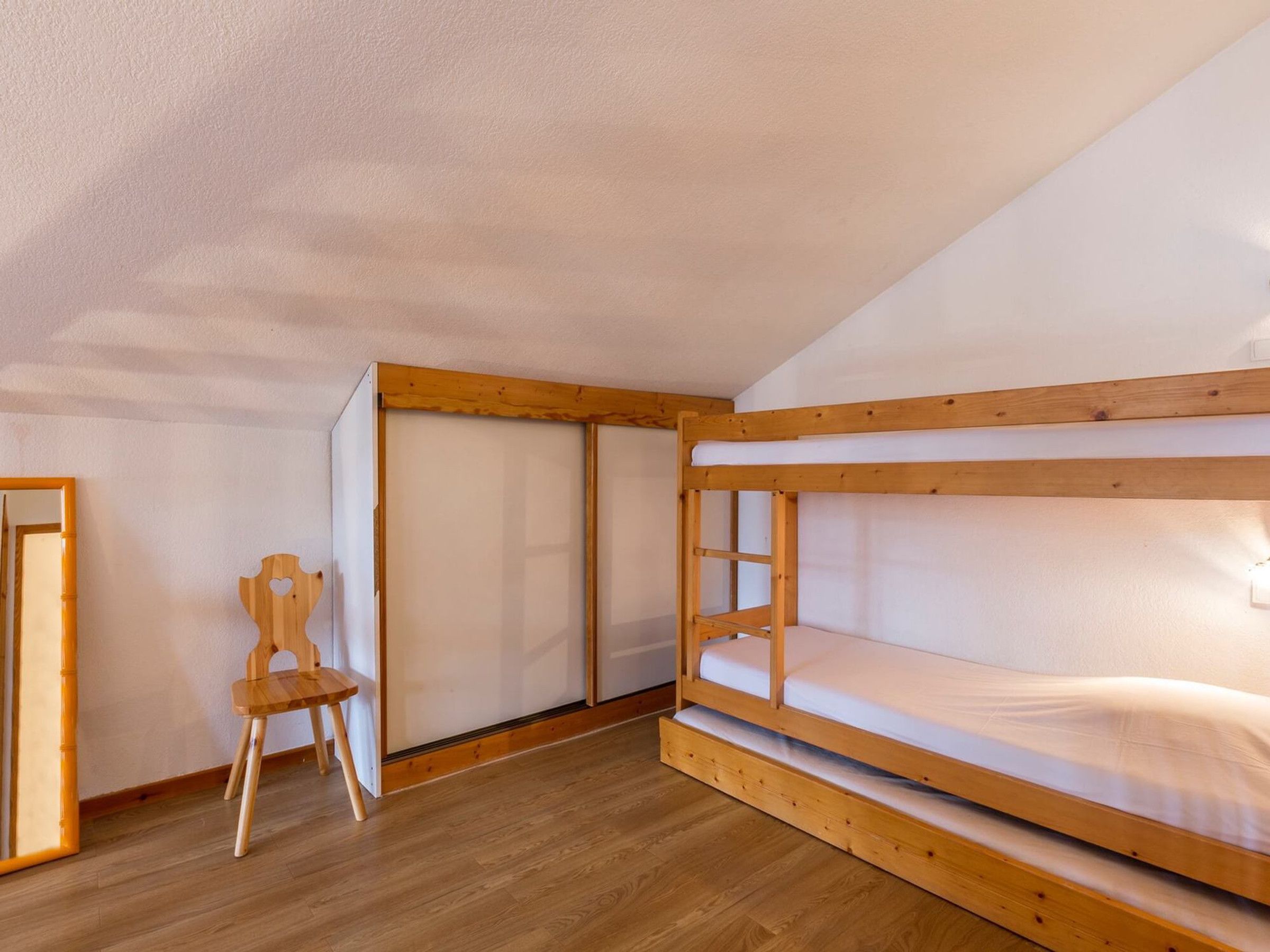 Habitación con literas, una silla de madera y una puerta corredera.