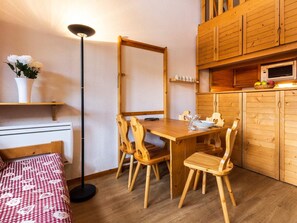 Ein gemütlicher Raum mit einem Holztisch, vier Stühlen, einer kleinen Küchenzeile mit einer Mikrowelle und einem Einzelbett mit einem gemusterten Überwurf.