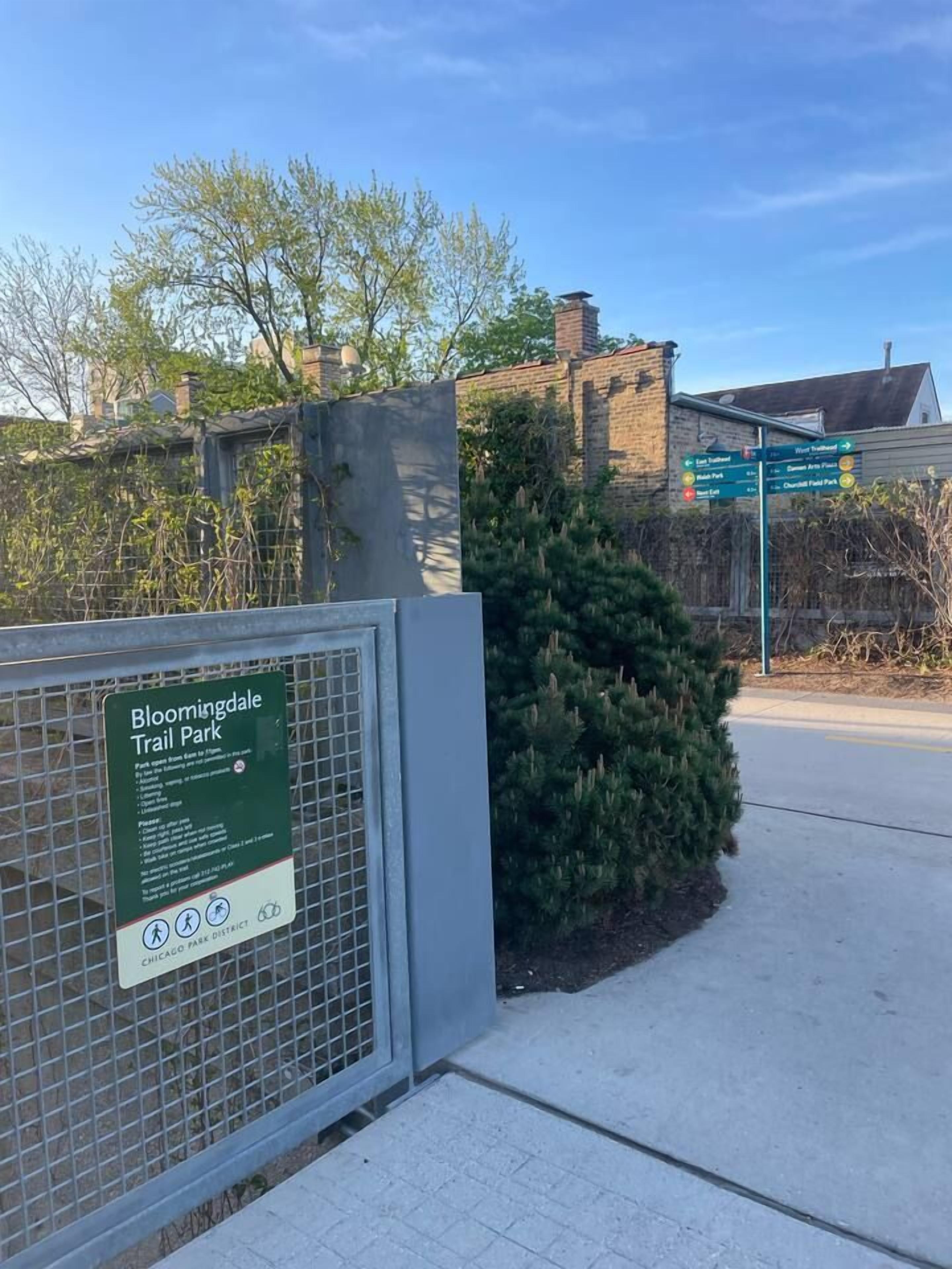 Un panneau indiquant l’entrée du parc Bloomingdale Trail, avec une clôture en métal et un buisson.