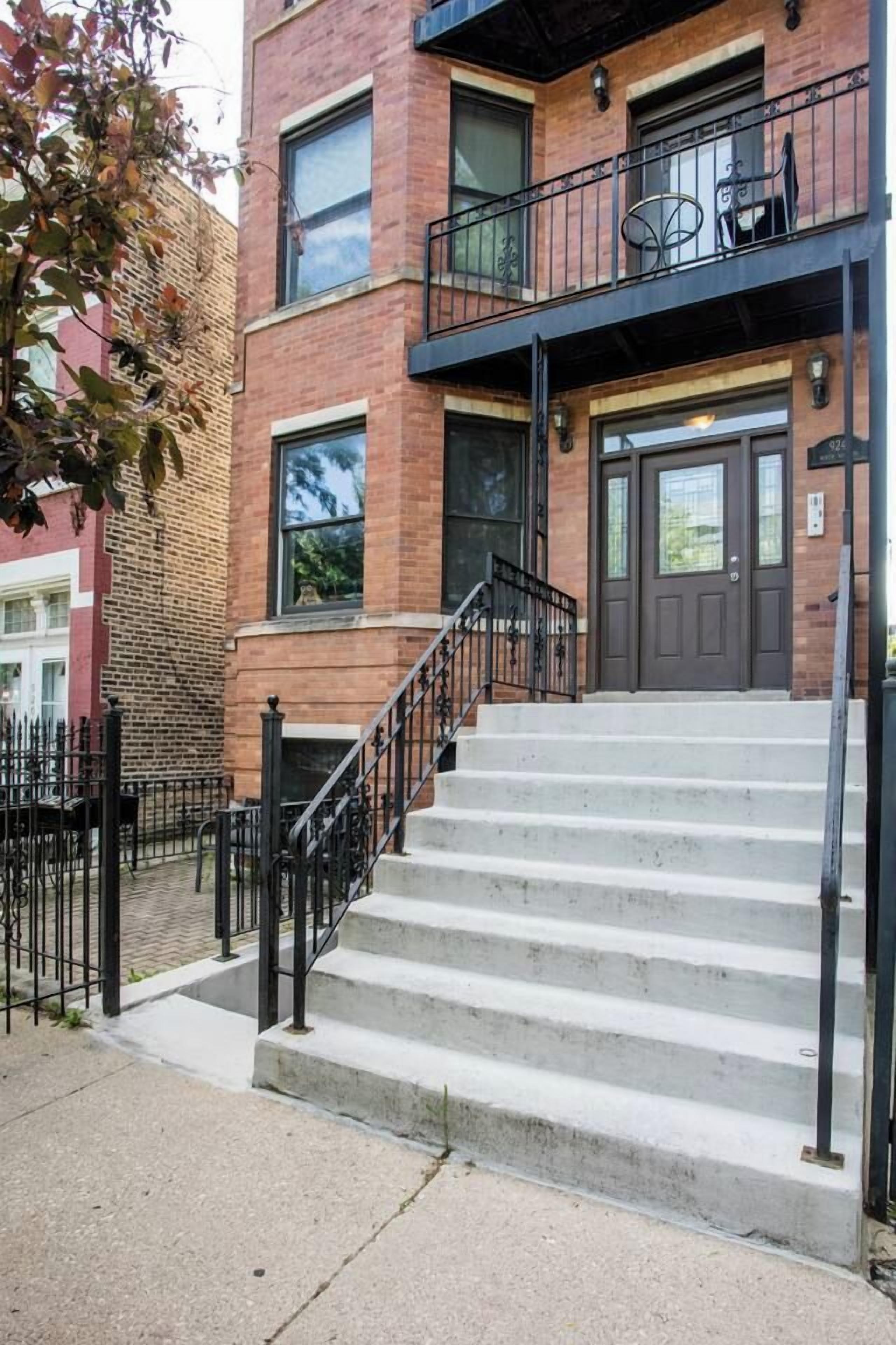 Un immeuble à plusieurs étages, doté d’une façade en briques, d’un escalier en métal noir et d’une entrée fermée par un portail.