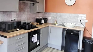 Una cocina moderna con armarios grises, encimera de madera, lavavajillas negro y un reloj en la pared.