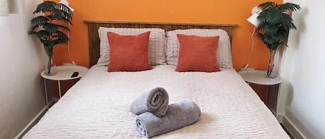 A hotel room with a bed, a round mirror on the wall, and two side tables with plants.