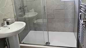 Un baño moderno con ducha envuelta en vidrio, lavamanos pedestal y retrete.