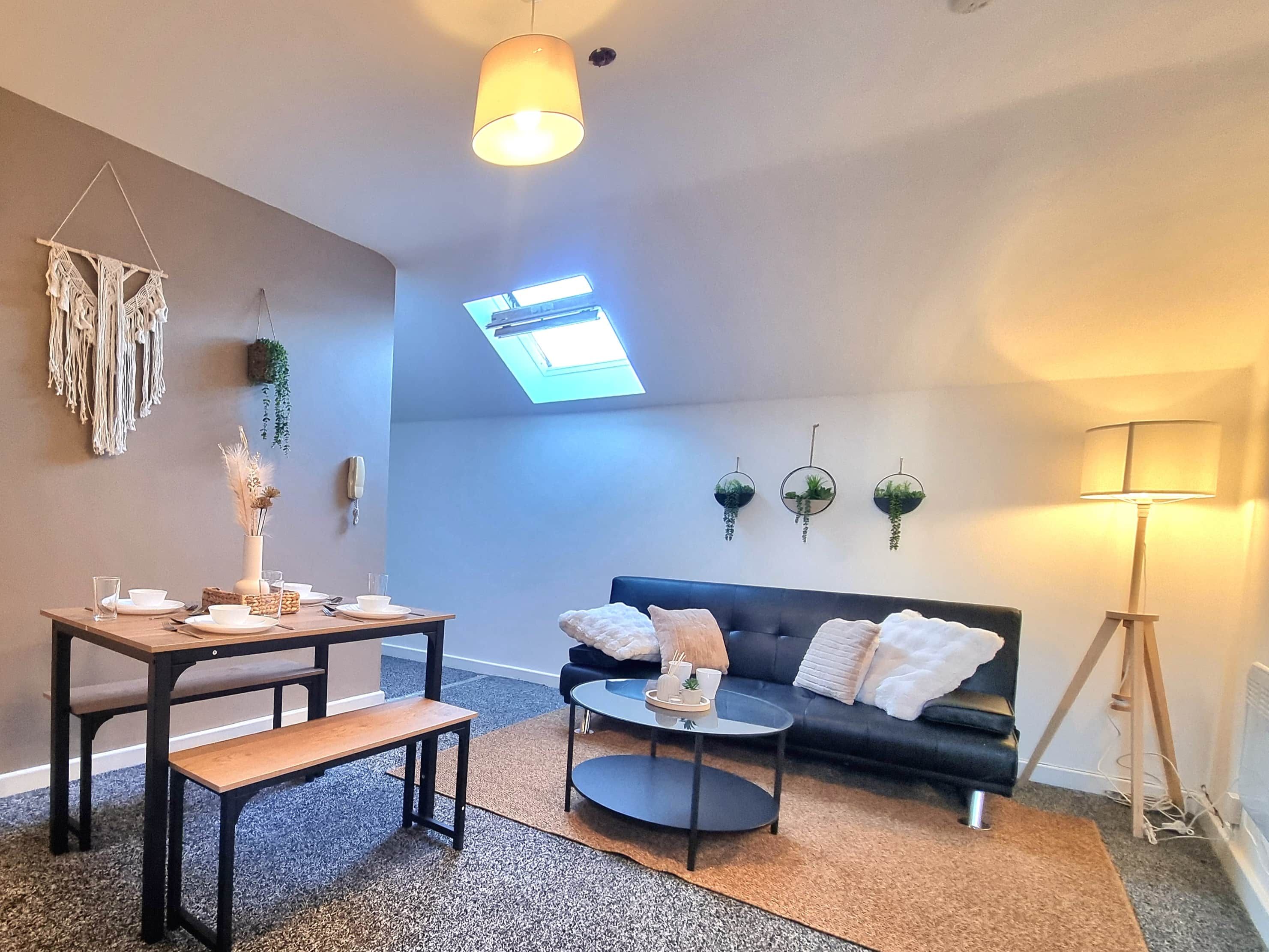 Un salón moderno con mesa de comedor, sofá y mesa de centro. Hay un tragaluz, plantas montadas en la pared y una lámpara.