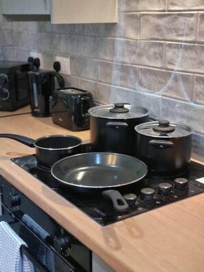 Una cocina con estufa, ollas, sartenes y un tostador.