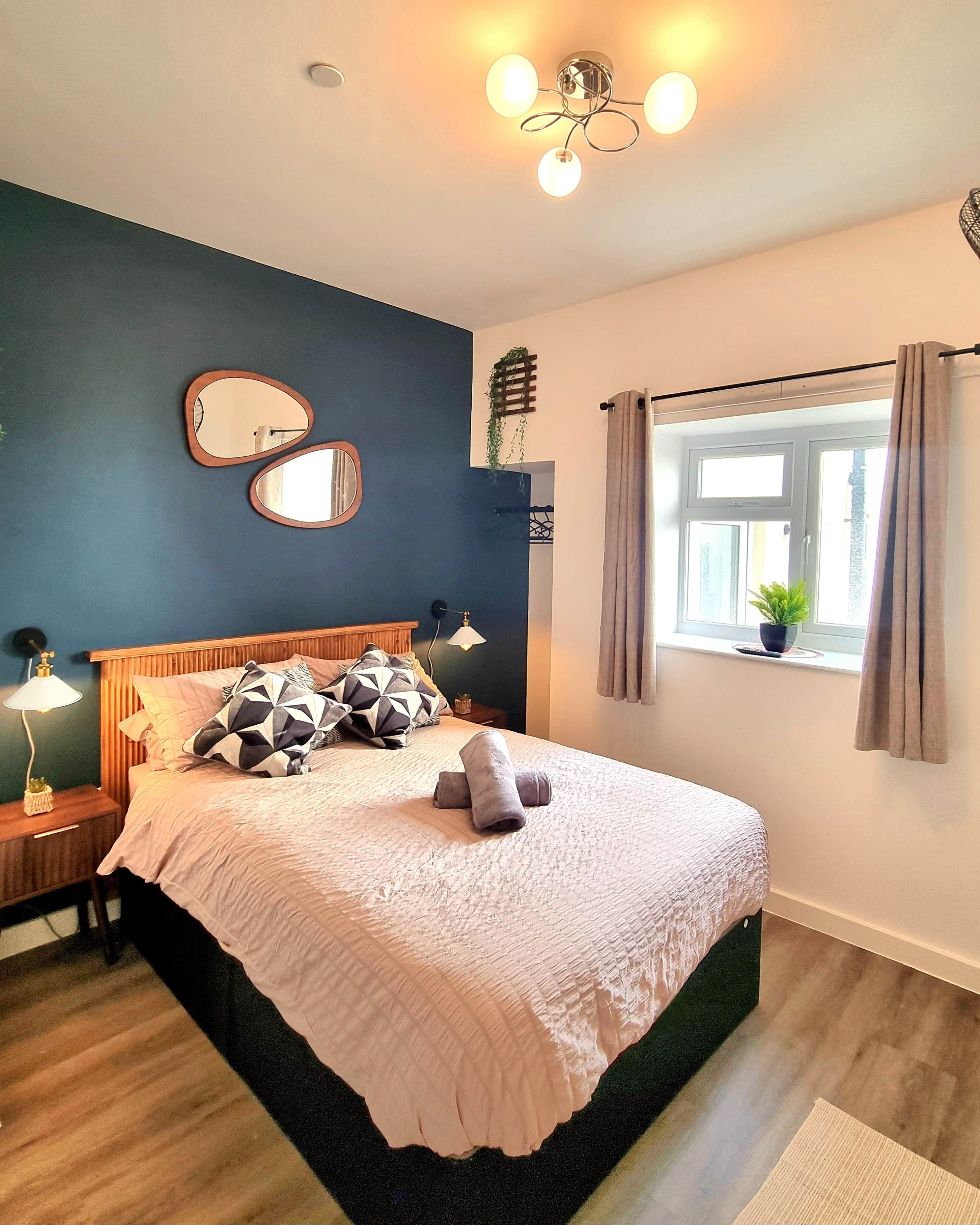 A bedroom with a bed, bedside tables, a window with curtains, and a ceiling light fixture.