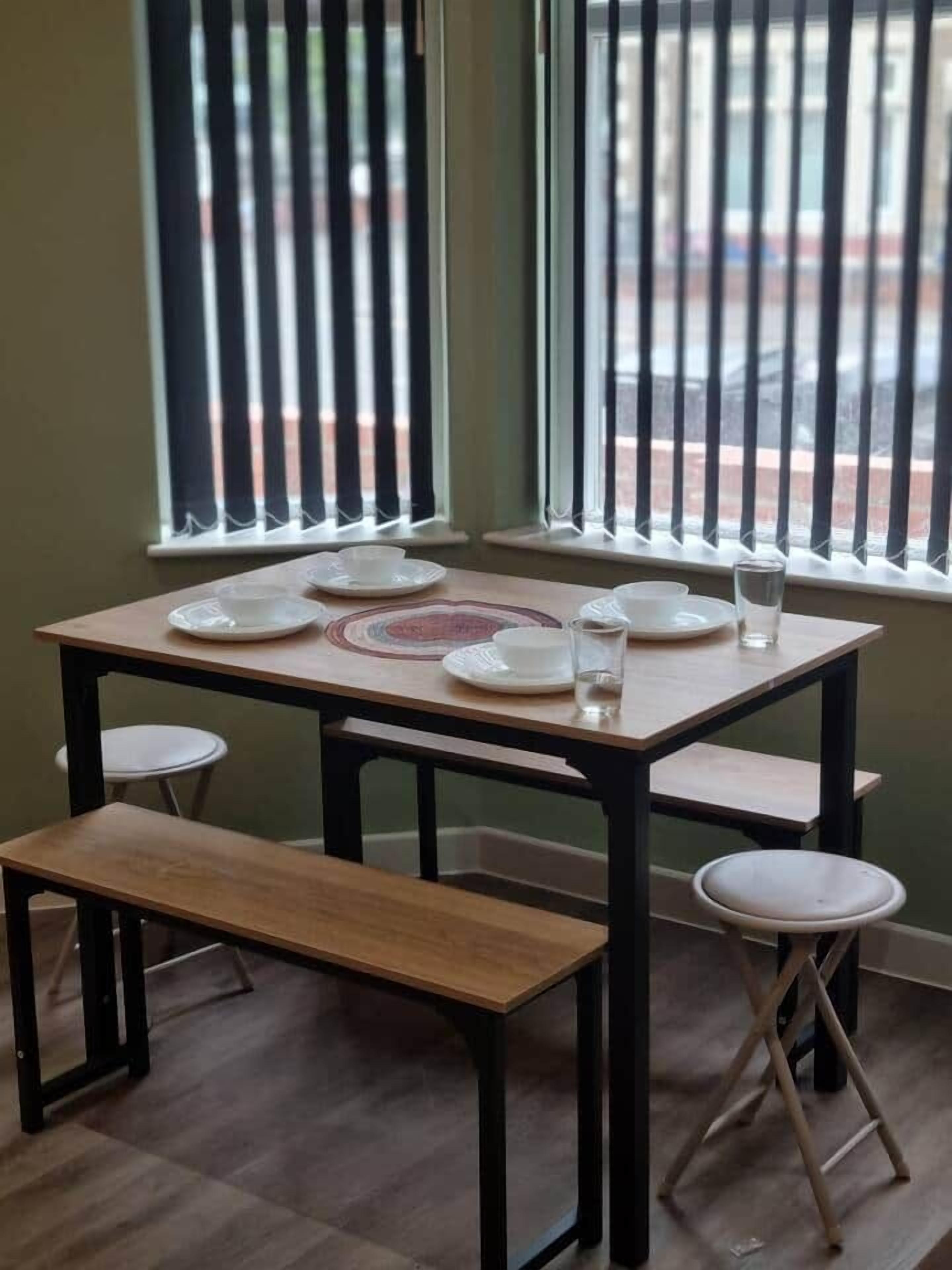 Une table à manger avec quatre chaises, un banc et une fenêtre avec des stores verticaux.