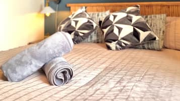 Una cama bien hecha con almohadas estampadas, un espejo en la pared y una lámpara de noche.