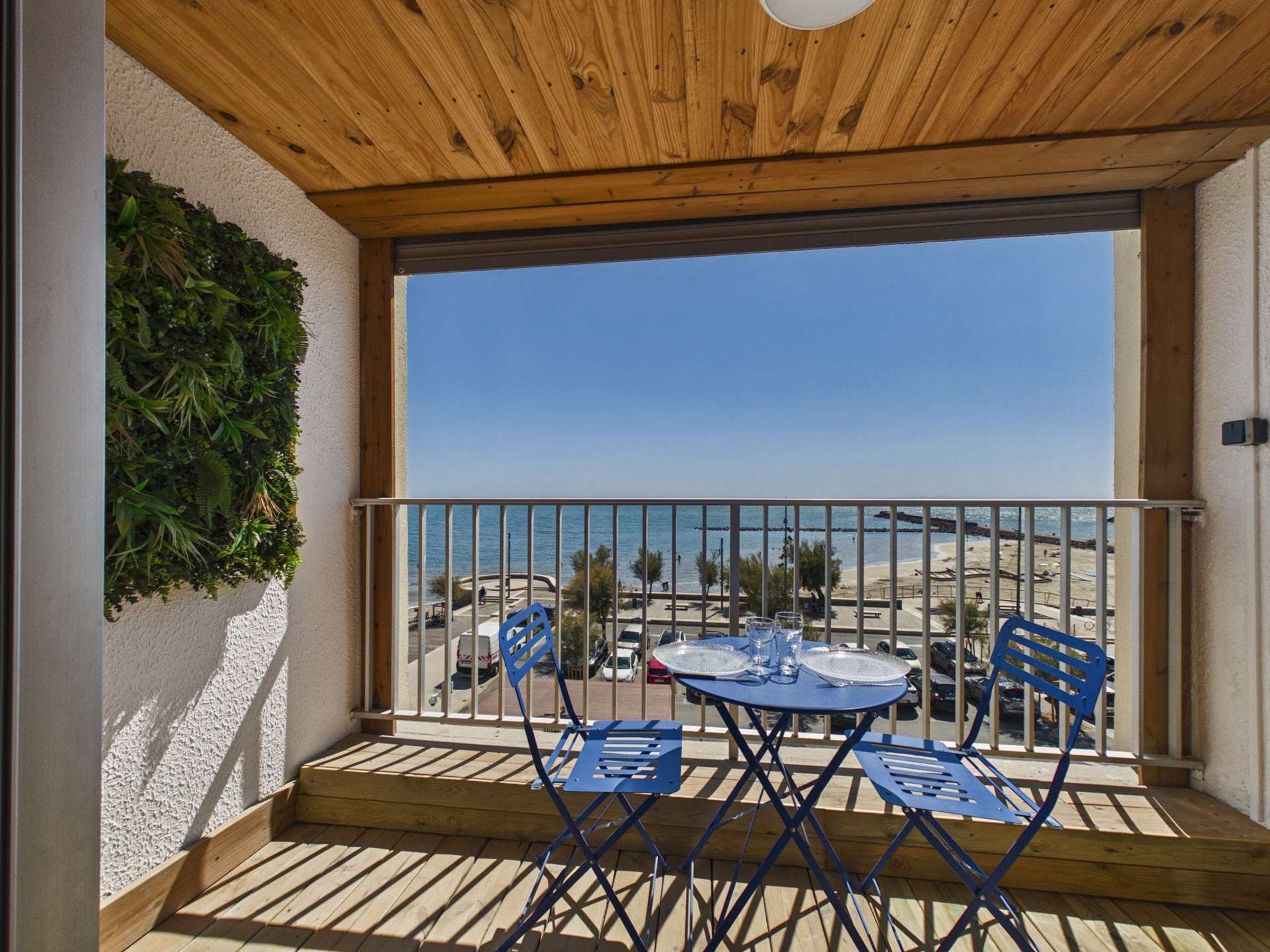 A balcony with a wooden ceiling, a view of the beach, and a table with chairs.