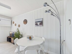Una habitación blanca con una mesa redonda, sillas blancas, un reloj de pared, un cuadro enmarcado y una lámpara de pie.