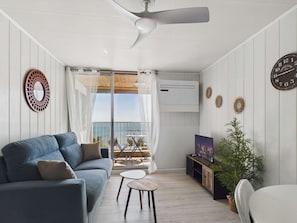 Una sala de estar con un sofá, una mesita, un mueble para televisión y un ventilador de techo.