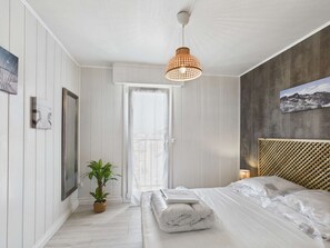 Ein Schlafzimmer mit einem Bett, einer Topfpflanze, einer Hängelampe und einer Tür zu einem anderen Raum.