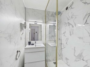 Ein modernes Badezimmer mit einer Duschkabine aus Glas, einem weißen Marmorwaschbecken und einem großen Spiegel.