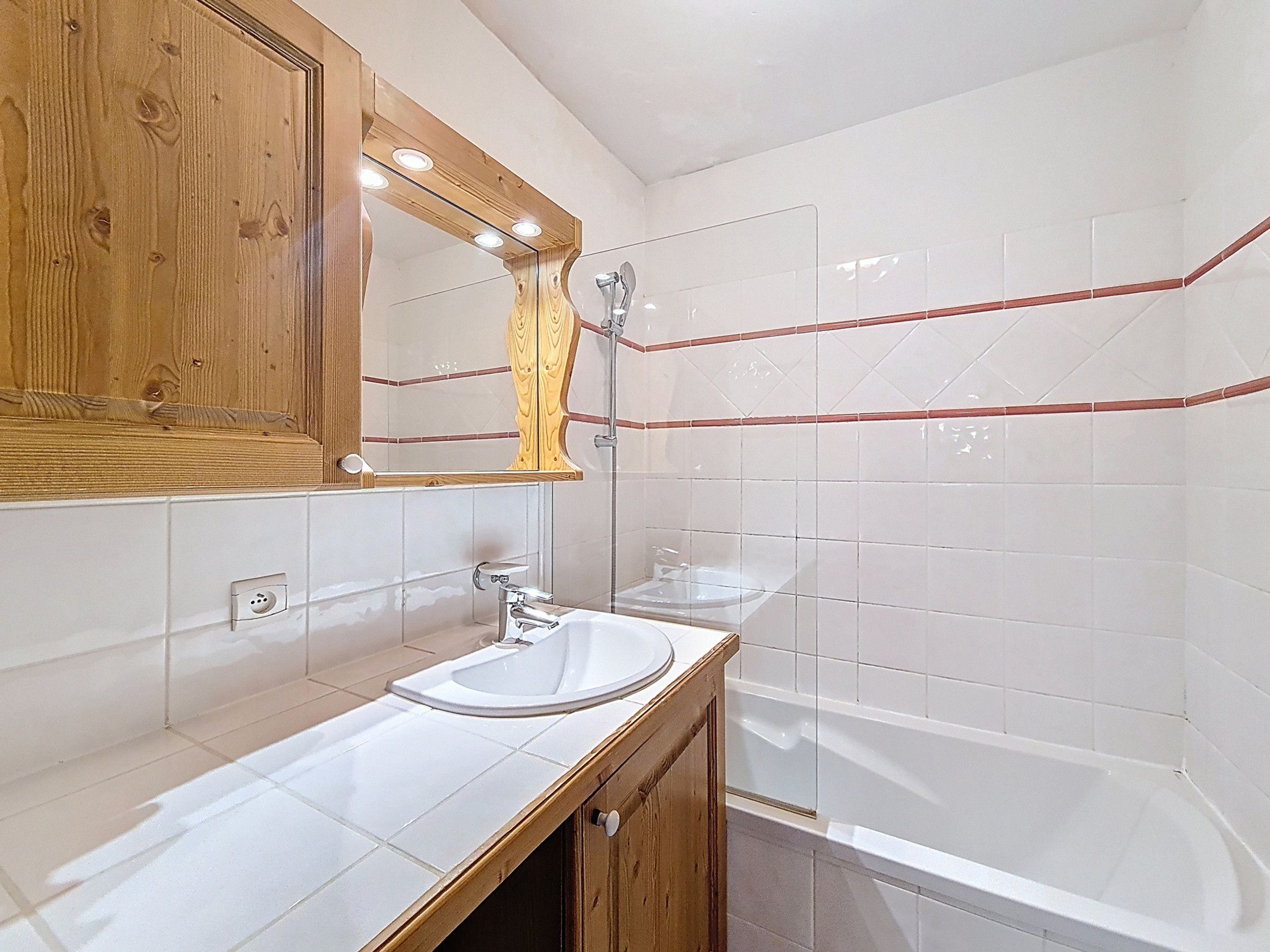 Ein Badezimmer mit einem Holzbadschrank, einem Spiegel, einem Waschbecken und einer Badewanne.