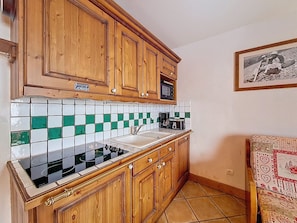 A kitchen with wooden cabinets, a tiled backsplash, a stove, and a coffee maker. - Les Menuires - 3 rooms, 6 pers, terrace, pool access (Les Menuires)