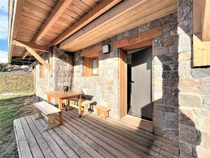 Ein Steinhaus mit einer Holzterrasse, einem Tisch und Bänken.
