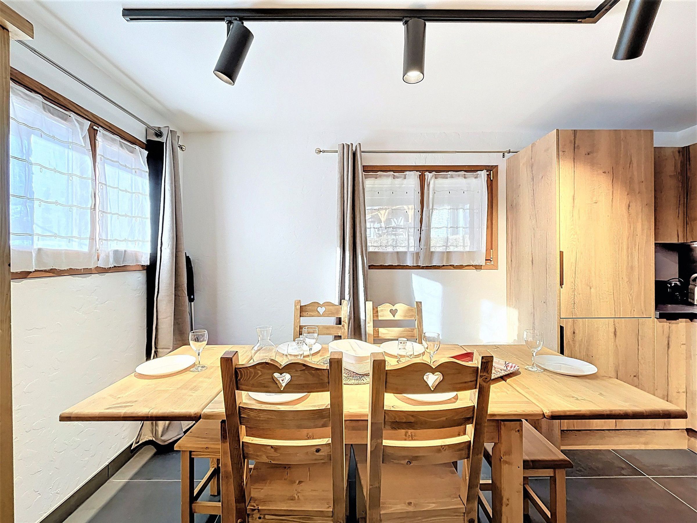 A dining area with a wooden table and chairs, a window with curtains, and a kitchen area with wooden cabinets.