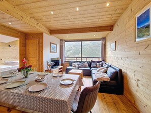 A wooden cabin interior with a dining area, sofa, and a large window offering a view of the outdoors. - Spacious apartment, 3 rooms, pets allowed, parking, Les Menuires (Les Menuires)