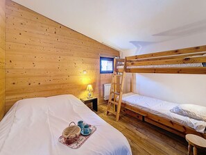 A room with wooden walls, a bunk bed, a bedside table with a lamp, and a window. - Spacious apartment, 3 rooms, pets allowed, parking, Les Menuires (Les Menuires)
