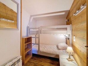A small, compact room with a bunk bed, a wooden shelf unit, and a bedside table with a lamp. - Spacious apartment, 3 rooms, pets allowed, parking, Les Menuires (Les Menuires)