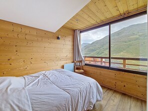 A bedroom with a large window, wooden walls, a bed, and a chair. - Spacious apartment, 3 rooms, pets allowed, parking, Les Menuires (Les Menuires)