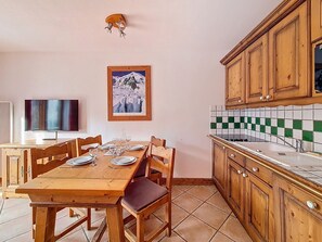 A dining area with a wooden table, chairs, and a television on the wall. - Spacious 3-room apartment near slopes with terrace, pool and parking (Les Menuires)