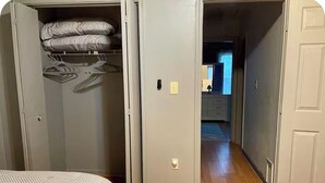 A bedroom with a bed, a closet with hanging clothes, and a hallway leading to another room. - Cozy Home Away From Home (Woodbridge)