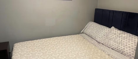 A bed with a patterned bedspread, a headboard, and a framed artwork on the wall.