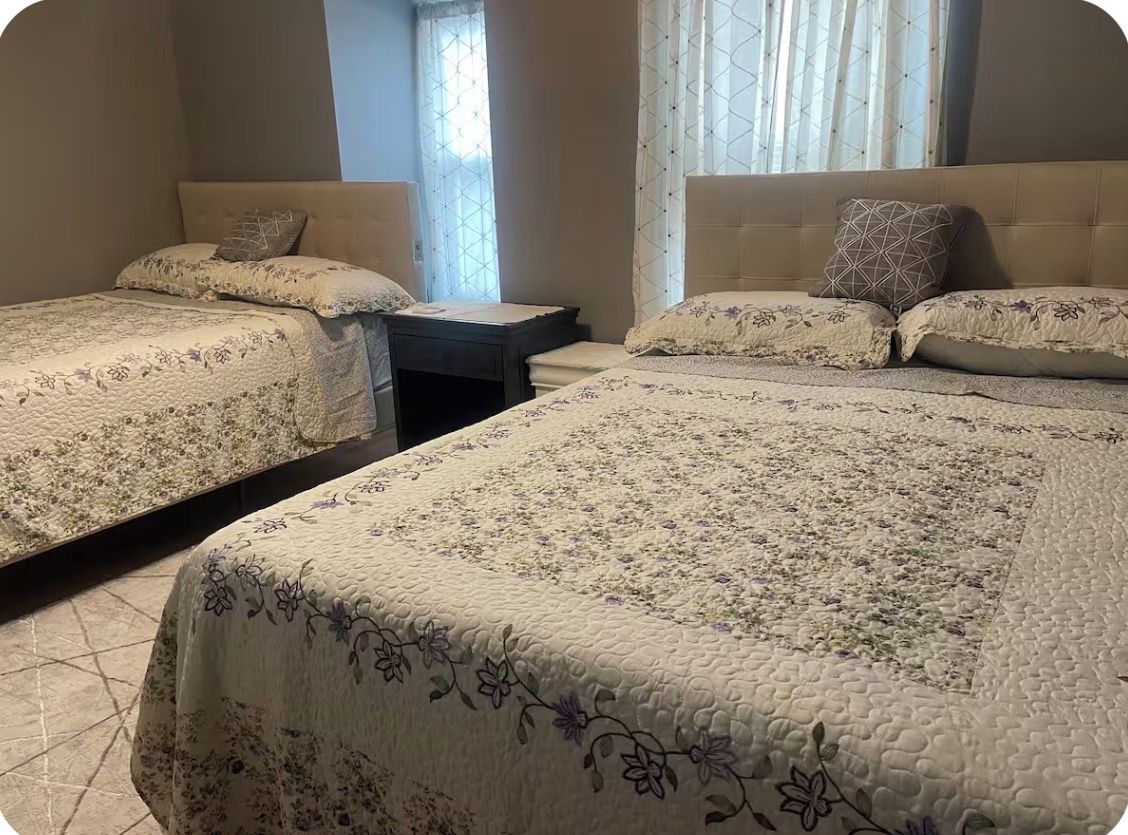 A hotel room with two beds, a nightstand, and a window with curtains.