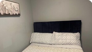 A bed with a patterned bedspread and pillows, a dark headboard, and a wall-mounted artwork of vases with flowers. - Cozy Home Away From Home (Woodbridge)