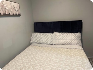 Ein Bett mit einem gemusterten Überwurf und Kissen, ein dunkles Kopfteil sowie ein Wandbild mit Vasen und Blumen.