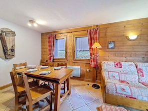 A wooden interior with a dining table set for four, a sofa, and a lamp. - Spacious apartment with balcony and parking, close to slopes (Les Menuires)
