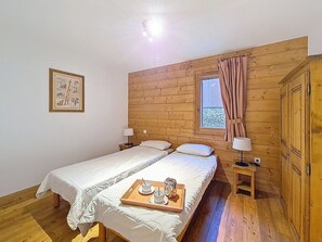 A room with two beds, a window with curtains, a wooden headboard, a framed picture on the wall, and a tray with cups and a teapot on the bed. - Spacious apartment with balcony and parking, close to slopes (Les Menuires)