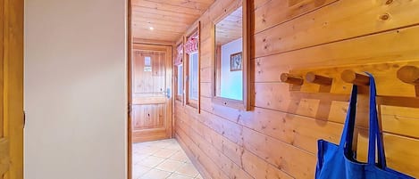 En hall med träpanel på väggarna, med en dörr som leder in till ett rum, ett fönster med utsikt och en blå väska med text på.