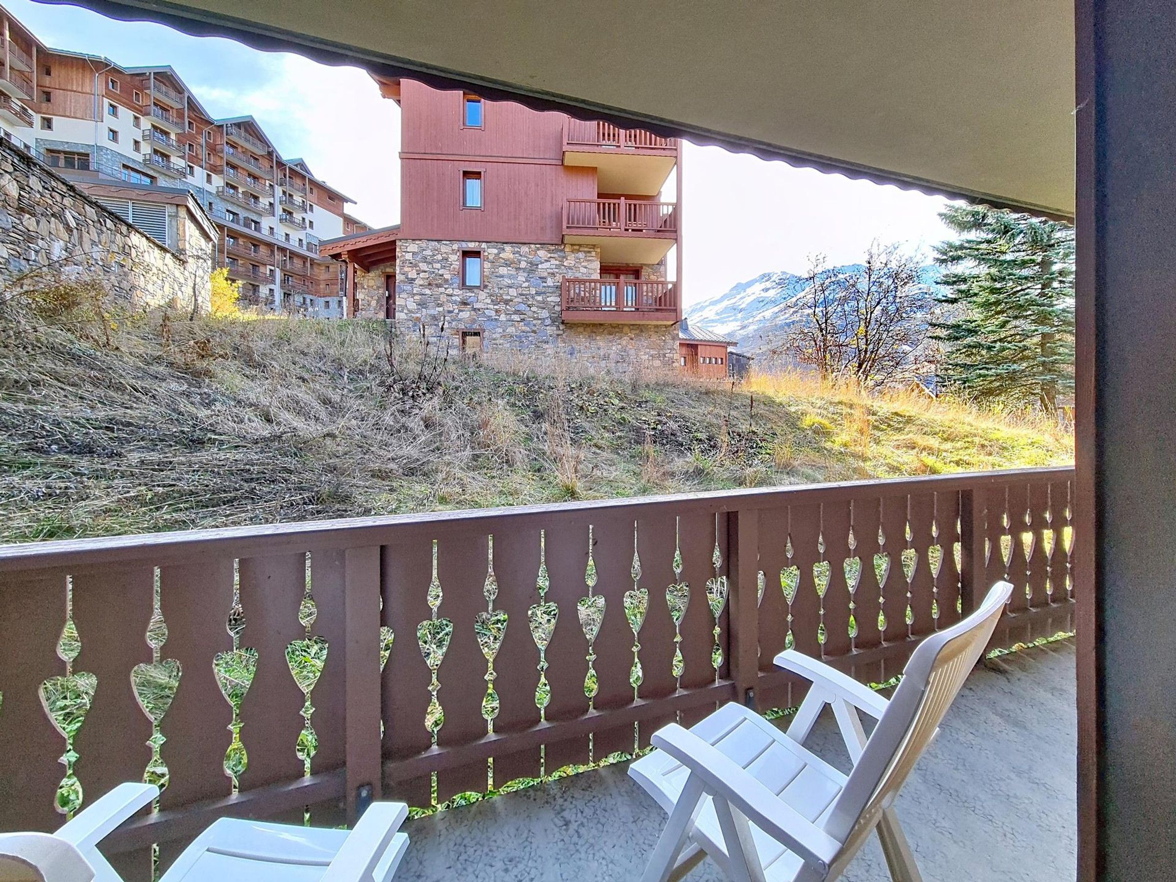 Un balcon offrant une vue sur une région montagneuse, des bâtiments en pierre et une clôture en bois.