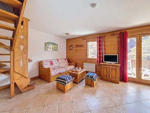 A cozy cabin with a wooden interior, a sofa, a television, and a window with curtains. - Spacious apartment in Menuires - Pool access included (Les Menuires)