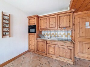 A kitchen with wooden cabinets, a tiled backsplash, and a black oven. - Spacious apartment in Menuires - Pool access included (Les Menuires)