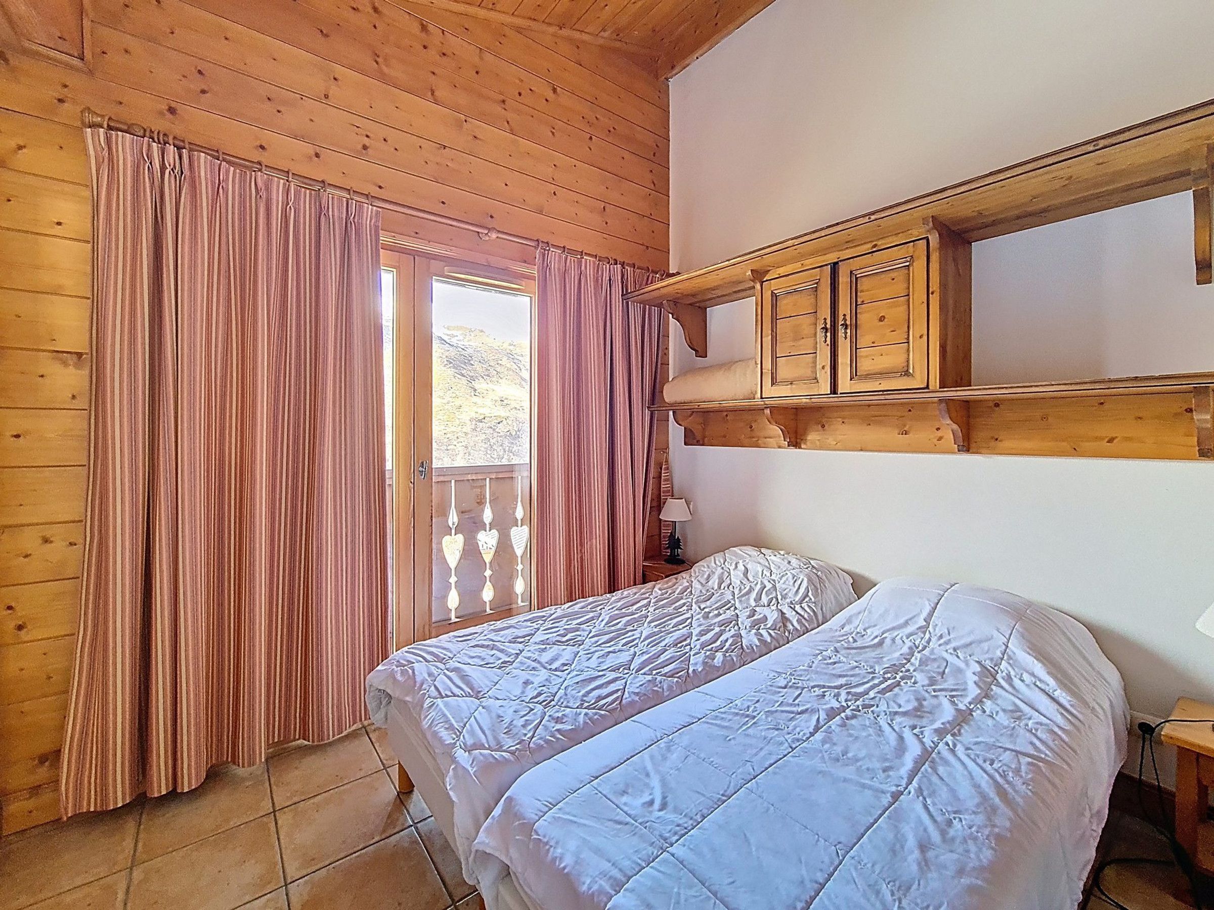 Een kamer met houten wanden en plafond, een bed met wit beddengoed, een houten kast en een raam met gordijnen.