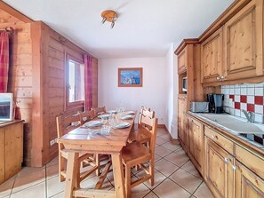 Ein Esszimmer mit einem Holztisch, Geschirr und Gläsern, Holzsesseln, Küchenschränken aus Holz, einer gefliesten Spritzschutzleiste und einer Deckenleuchte.