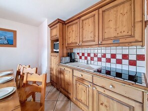 Cozinha com armários de madeira, painel de azulejos e área de jantar com cadeiras e mesa.