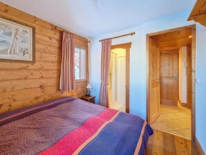A wooden room with a bed, a window, and a door leading to a bathroom. - Spacious apartment for 6 with pool access (Les Menuires)