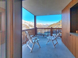 A balcony with two white chairs, a wooden railing, and a view of snow-covered mountains. - Spacious apartment for 6 with pool access (Les Menuires)