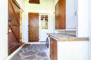A stone-floored entrance with wooden doors and a washing machine. - Villa Subera - à 2 min du lac d'Hossegor (Hossegor)
