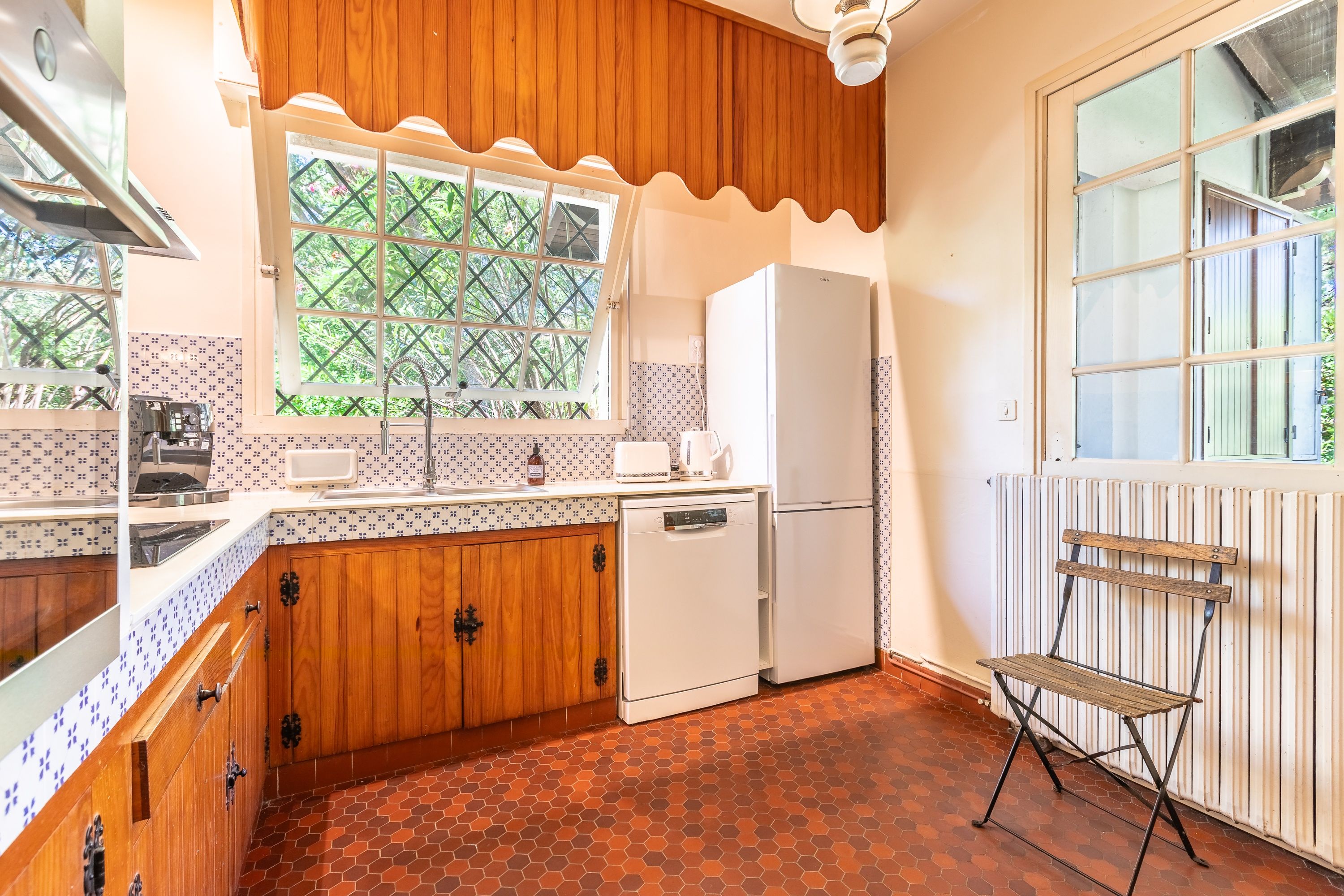 Une cuisine de taille réduite, avec des meubles en bois, un réfrigérateur blanc et une fenêtre donnant sur un paysage verdoyant.