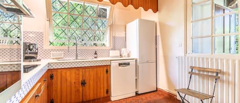 Une cuisine de taille réduite, avec des meubles en bois, un réfrigérateur blanc et une fenêtre donnant sur un paysage verdoyant.