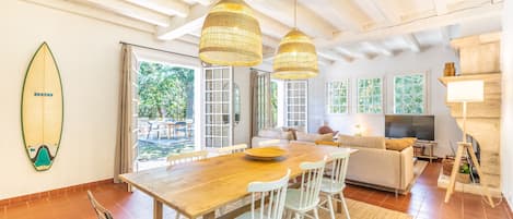 Un vaste espace de vie comprenant une table à manger en bois, des chaises blanches, un canapé et un téléviseur.
