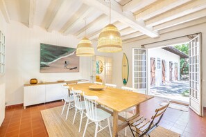 A dining area with a wooden table, white chairs, and a large painting of a beach scene. - Villa Subera - à 2 min du lac d'Hossegor (Hossegor)