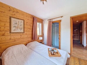 Une pièce aux murs lambrissés, avec un lit, un tableau encadré accroché au mur et un plateau contenant des tasses et une théière posé sur le lit.
